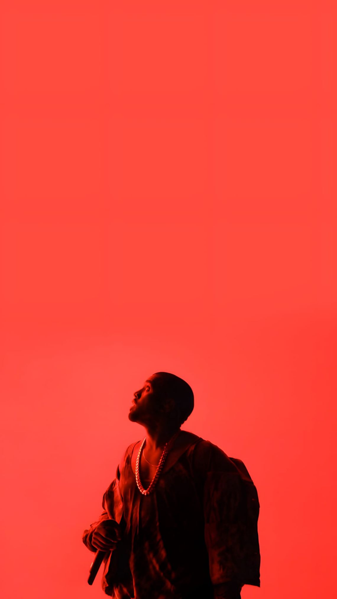 Kanye West on stage during the Yeezus Tour, bathed in red light, wearing a draped Maison Martin Margiela coat, looking upward