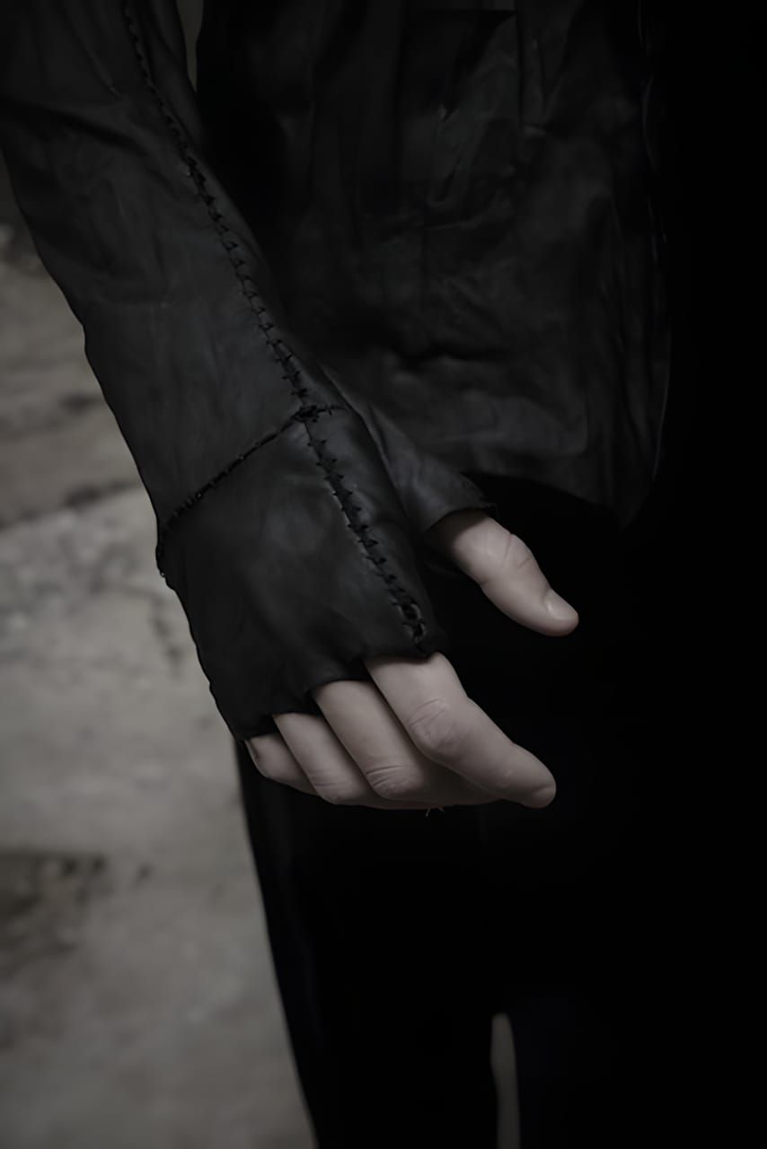 Close-up of a hand wearing a black leather fingerless glove gauntlet with visible hand-stitching along the seam, integrated w