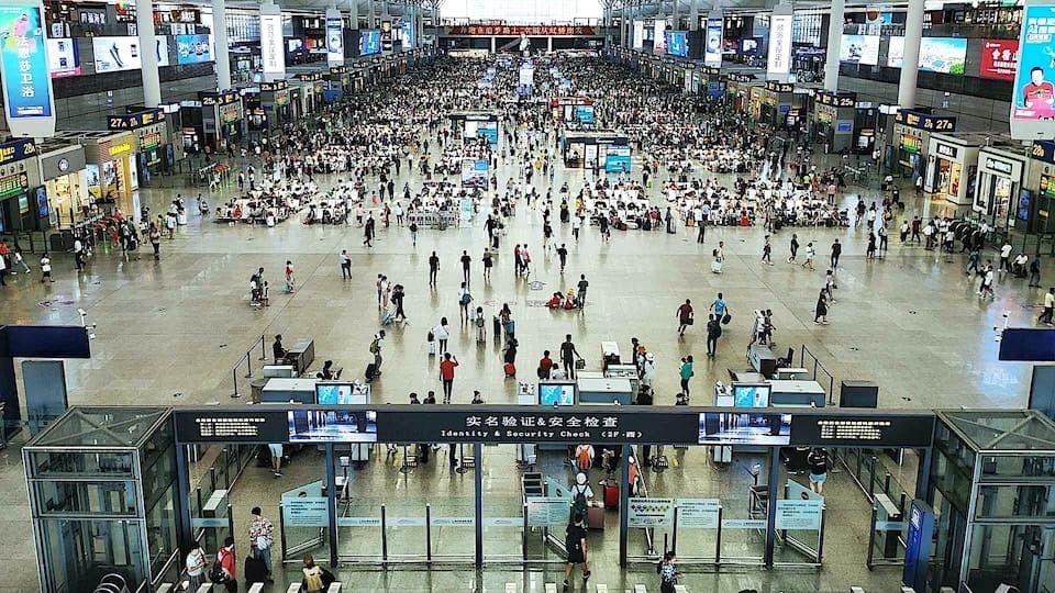 Crowded airport terminal with passengers moving through security and waiting areas.
