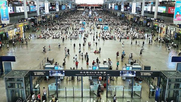 Crowded airport terminal with passengers moving through security and waiting areas.