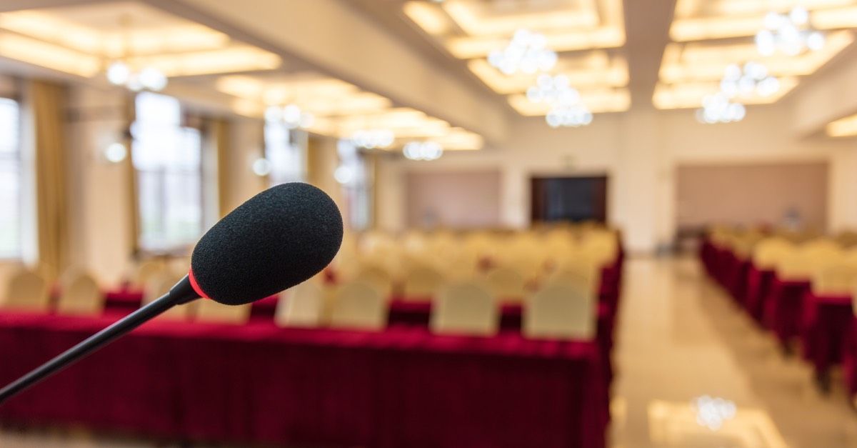 An empty function room, with a microphone in focus in the foreground, and empty seating out-of-focus in the background