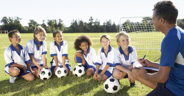 A football coach kneeling on a football pitch talking to a group of six children