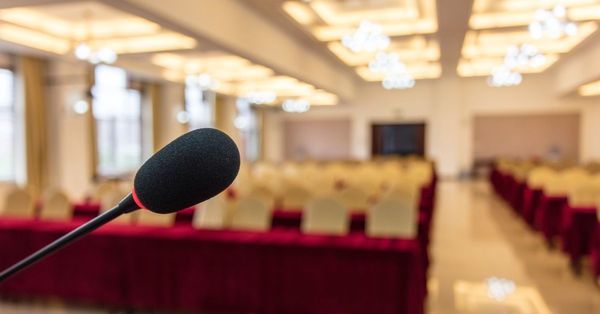 An empty function room, with a microphone in focus in the foreground, and empty seating out-of-focus in the background