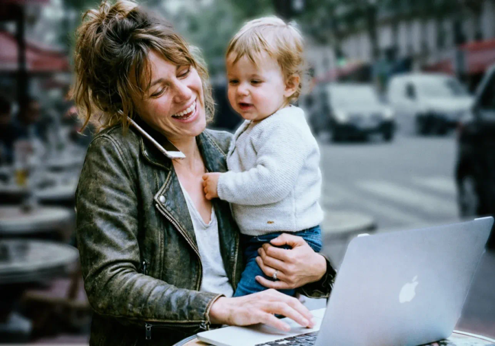 Une femme tenant un enfant tout en étant au téléphone et en tapant sur son ordinateur