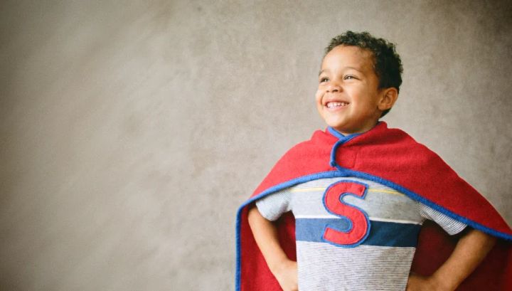 Un enfant se tenant droit et souriant. il regarde au loin et porte une cape faite d'une couvertur