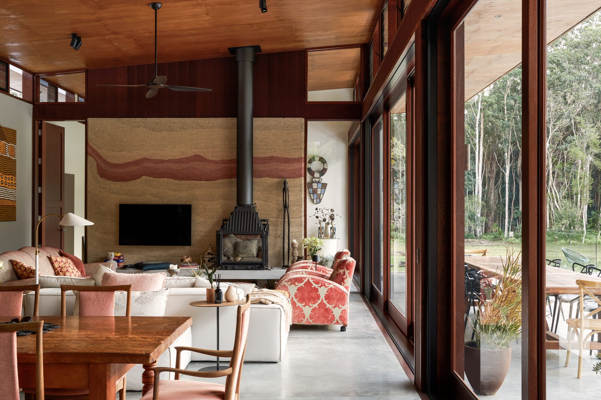 Modern tropical interior living space in earthy hues with hempcrete wall and wooden framed, sliding, glass doors.