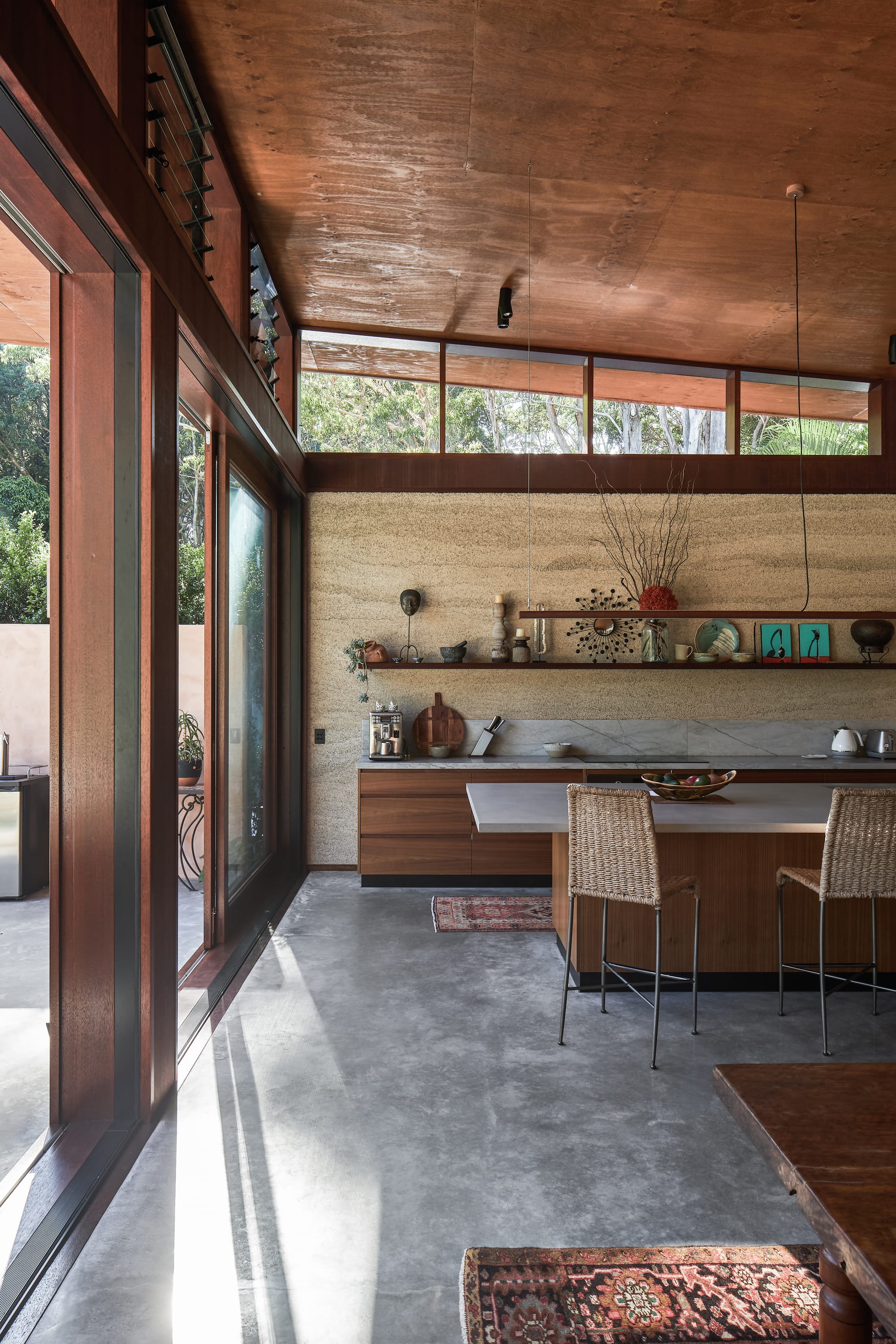 Modern interior architecture kitchen with rattan high chairs, middle eastern carpets and hempcrete wall in earthy hues.