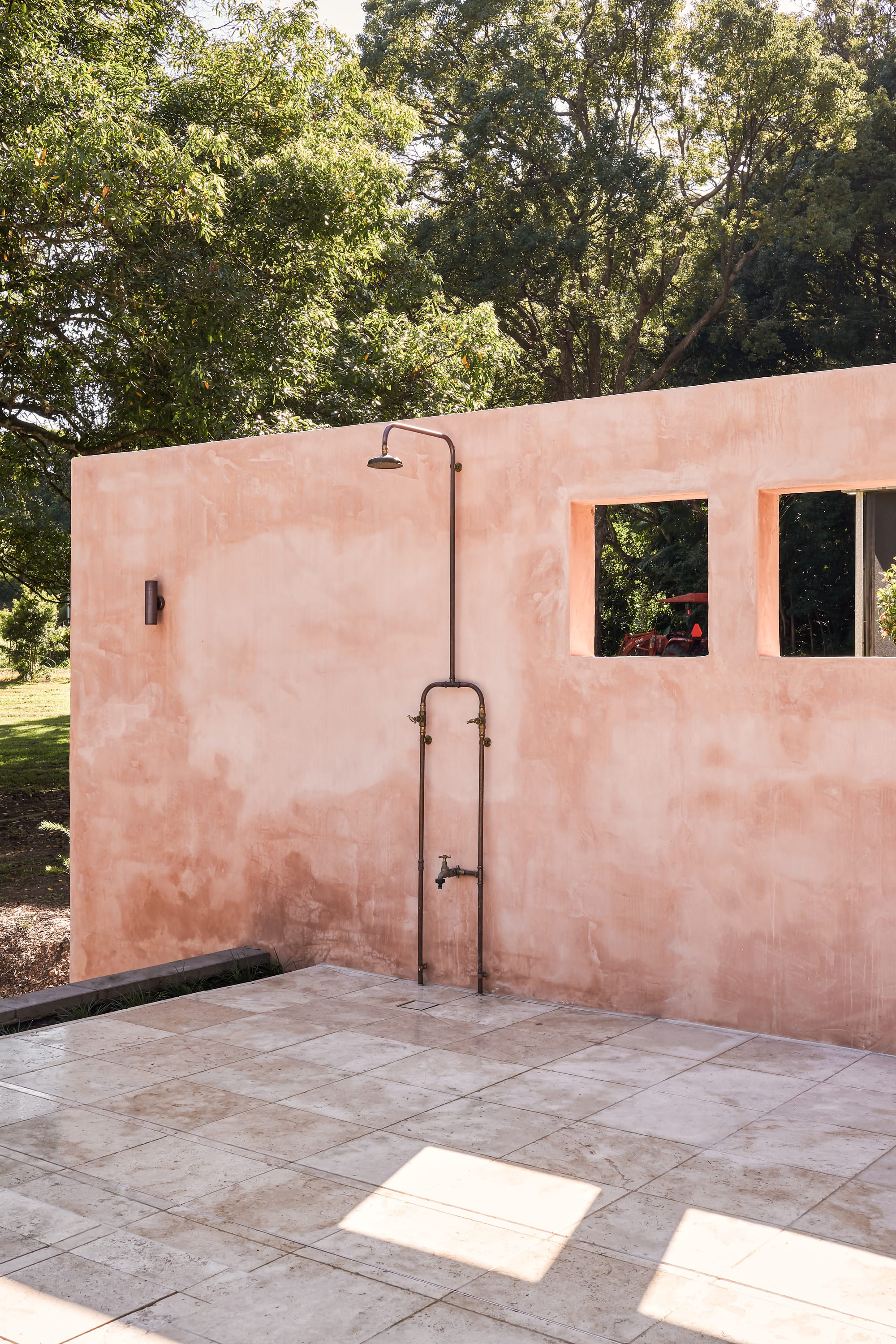 Terracotta painted wall with shower and small, squared windows pointing to surrounding trees.
