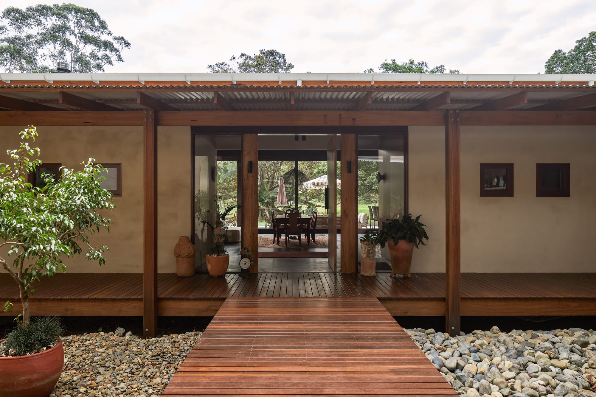 View on modern, tropical architecture with wooden walkway entrance and glass door.