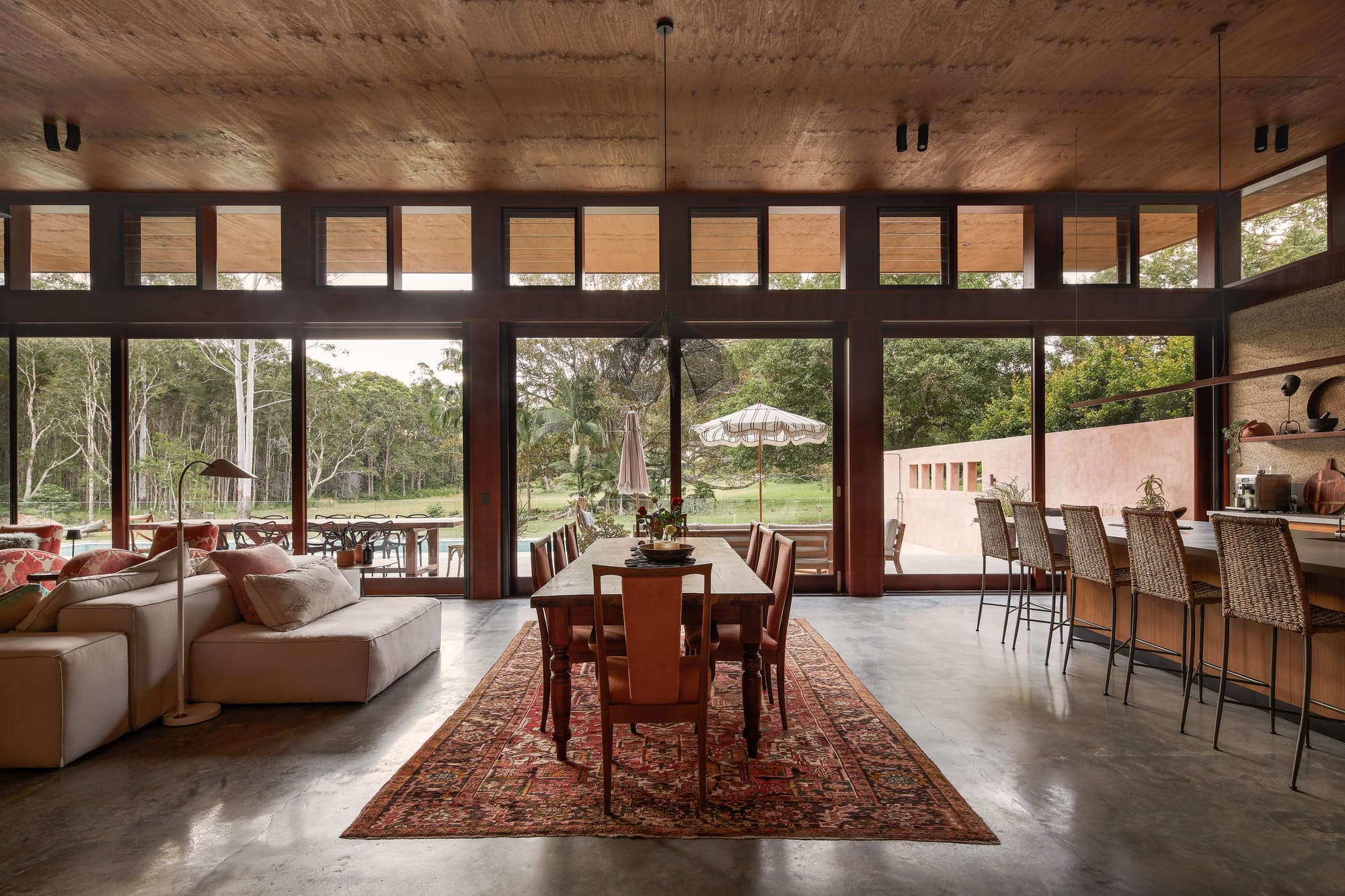 Modern, tropical interior architecture with smoothed screed, wooden ceiling and glassed panoramic window frames in earthy hues.