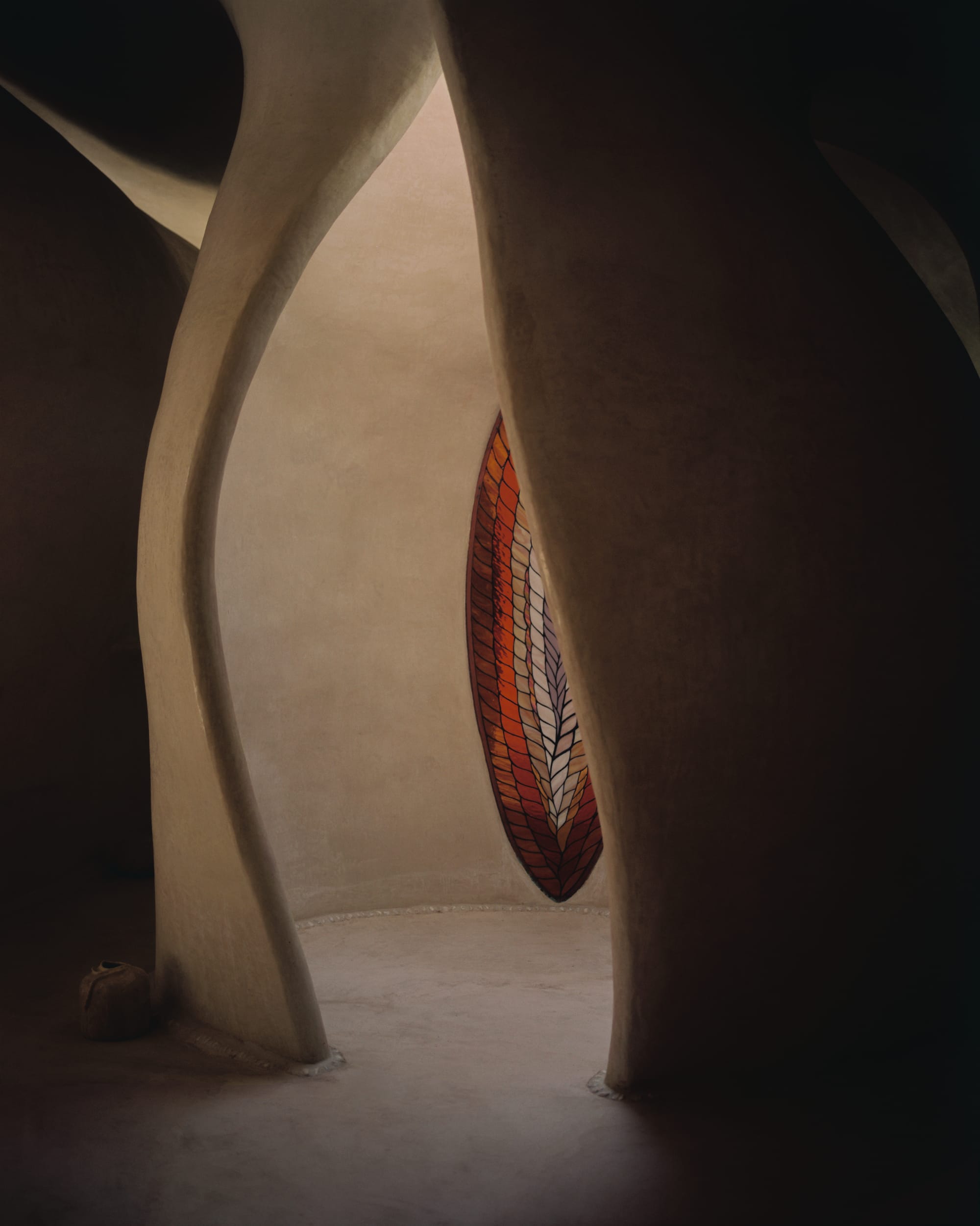 Interior space of organically shaped healing architecture with leaf shaped, stained glass window.