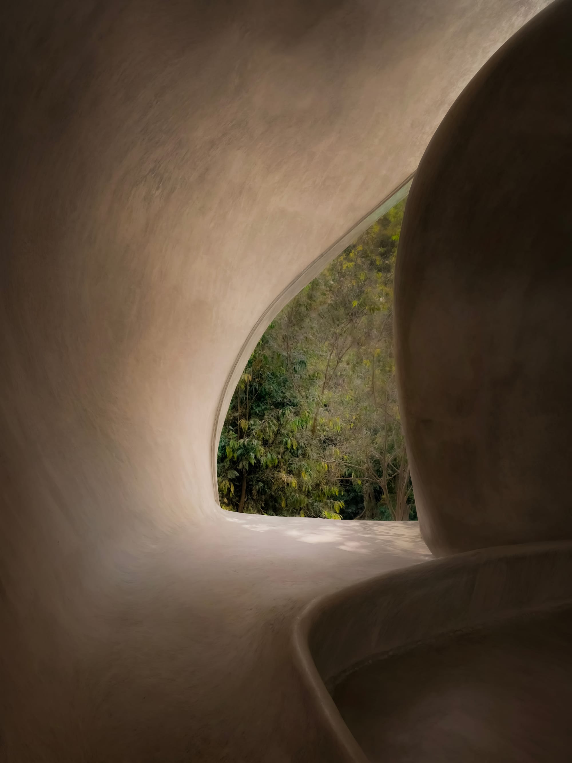 Organically shaped architectural interior space with monolithic approach, seamless integrated bench and organically shaped opening to lush jungle.