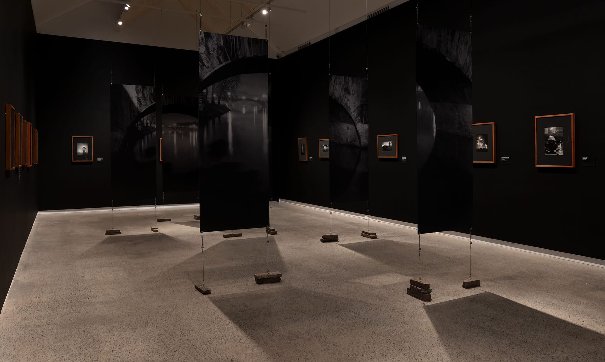Black gallery space showcasing photography and enlarged sectioned canvas in center.