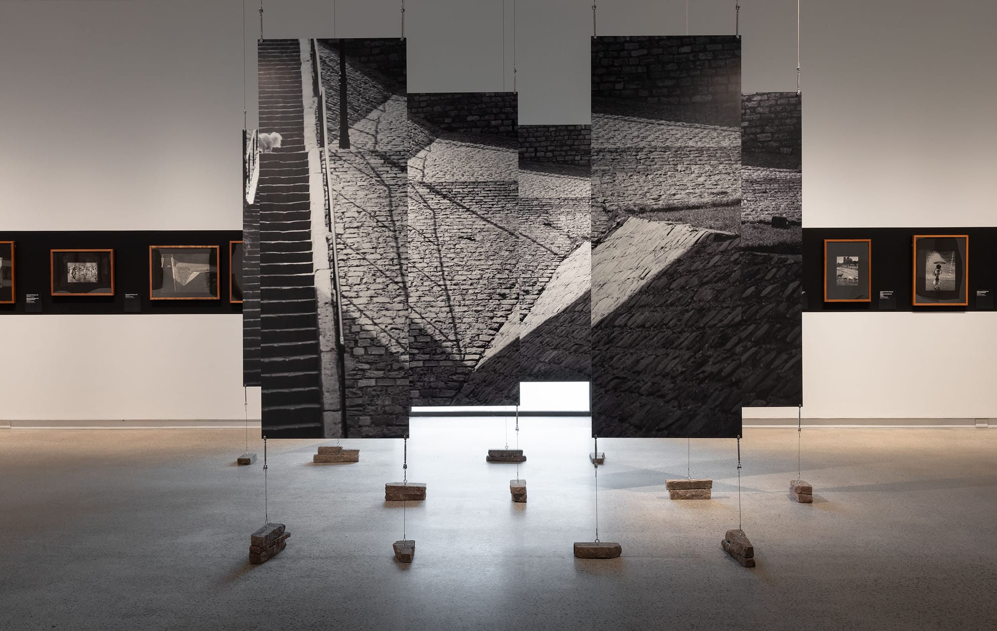 White gallery space showcasing photography and enlarged sectioned canvas in center.
