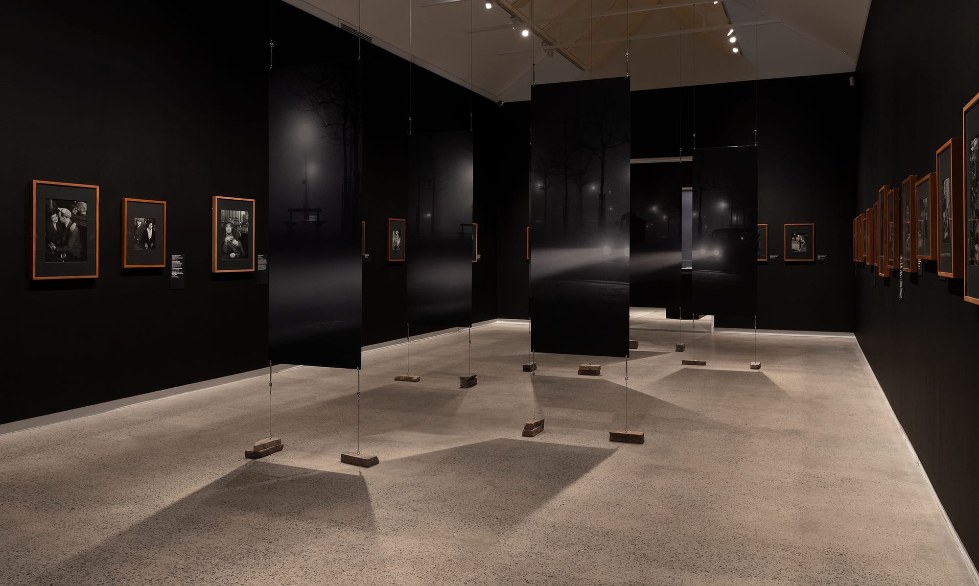 Black gallery space showcasing photography and enlarged sectioned canvas in center.