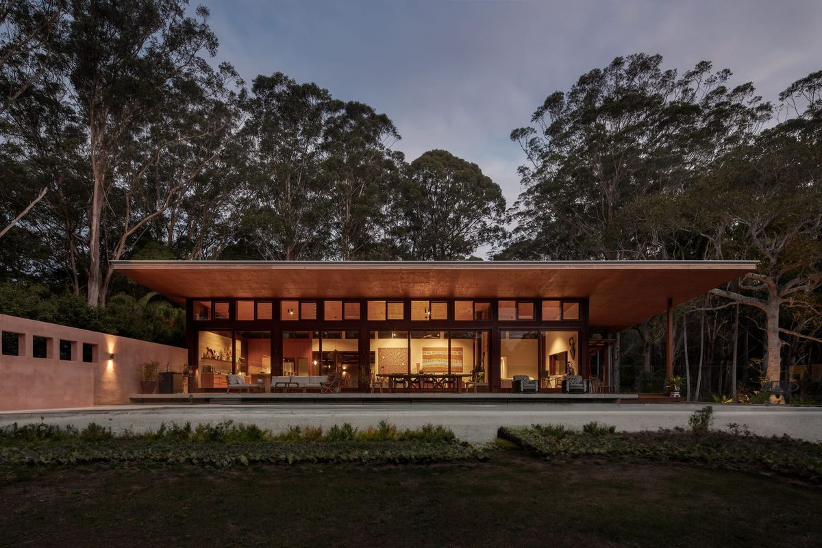 Outside evening view on modern, tropical family home, warm light with wooden facade and flat roof.