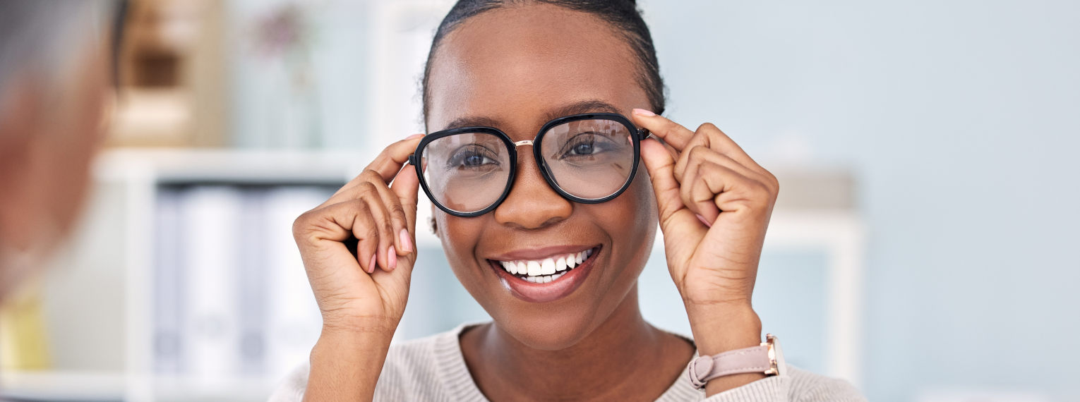 Eine Frau setzt eine Brille auf und lächelt dabei.