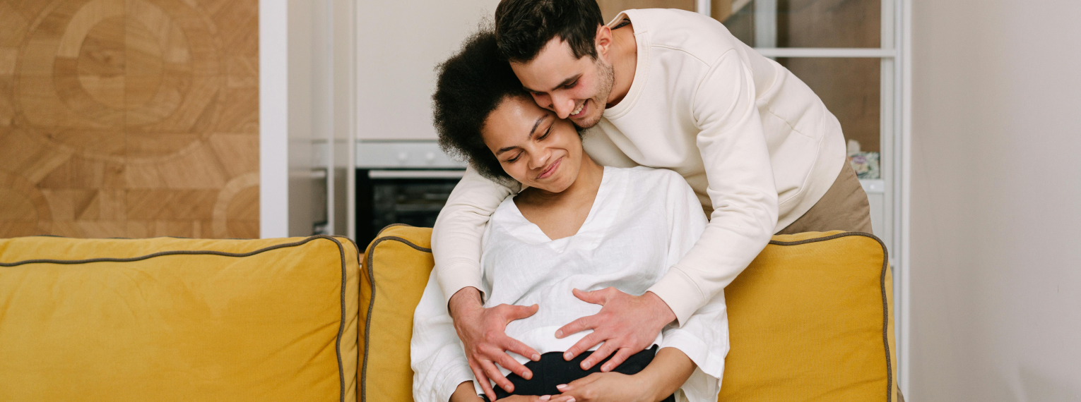 Eine schwangere Frau und ihr Partner halten ihre Hände an den Babybauch der Frau.