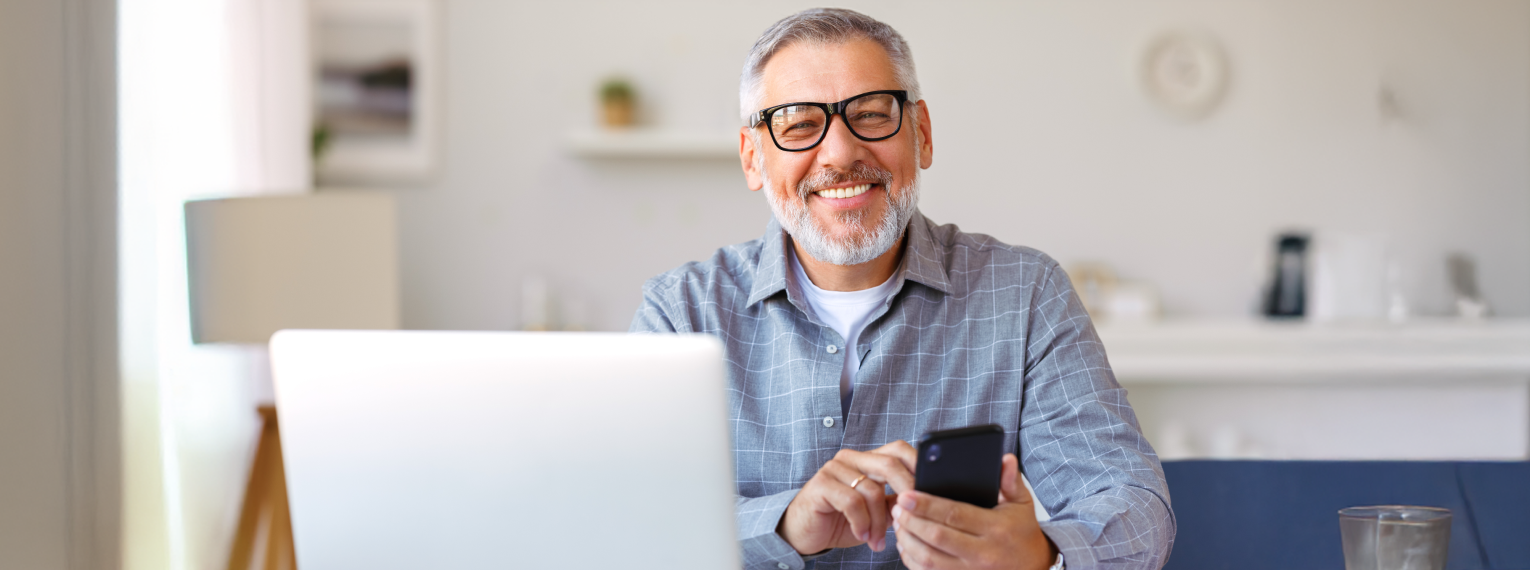 Ein Mann mit Brille lacht in die Kamera, während er sein Handy in der Hand hält.