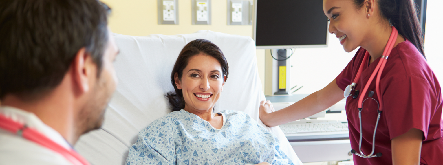 Eine Patientin in einem Krankenhaus-Einzelzimmer redet mit medizinischem Fachpersonal.