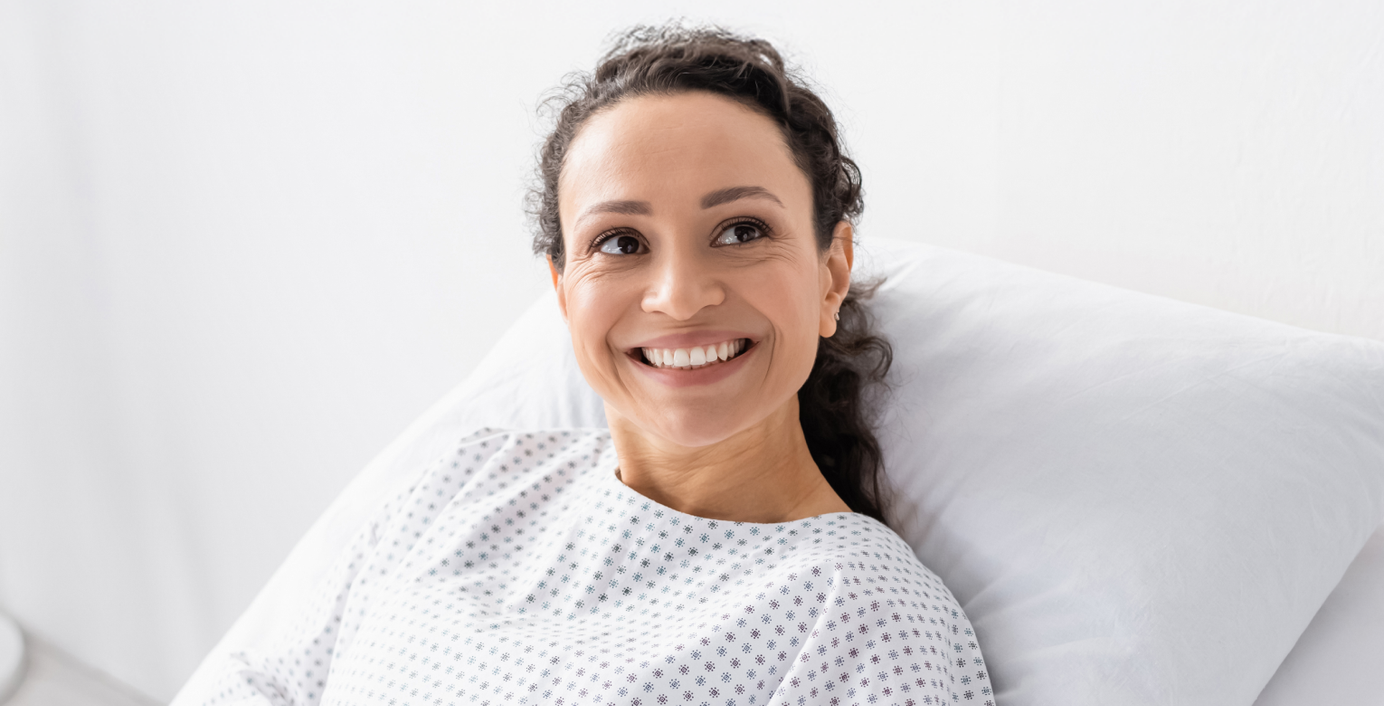 Eine Patientin in einem Krankenhaus-Einzelzimmer lächelt.
