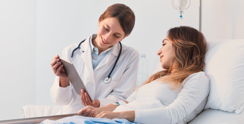 Eine Patientin im Krankenhausbett bespricht die Ergebnisse einer Untersuchung mit einer Ärztin