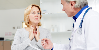 Eine Patientin mit Halsschmerzen erklärt einem Arzt ihre Symptome.