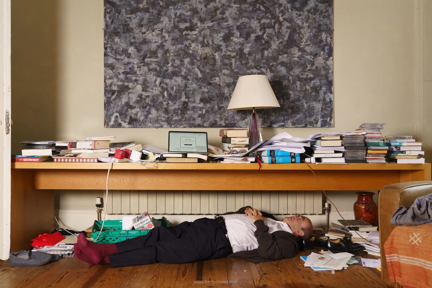 Colm Tóibín lying down underneath his desk, writing.