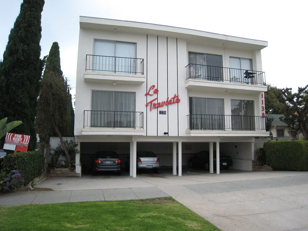 A cheap boxy apartment building with two stories of housing on top of four open parking spots with thin pillars
