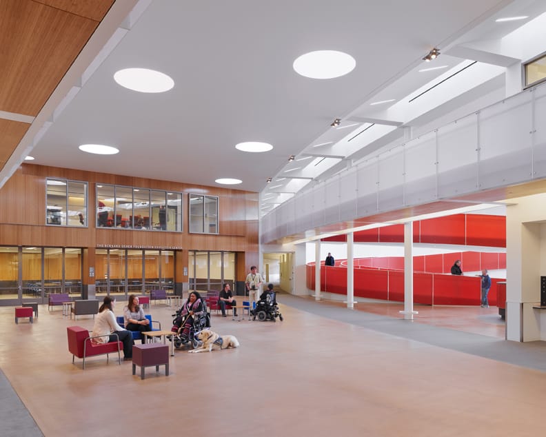 Wide open lobby of a two-story office building. People with different disabilities in the foreground. Red spiral ramp in the background. Downstairs and upstairs conference room.