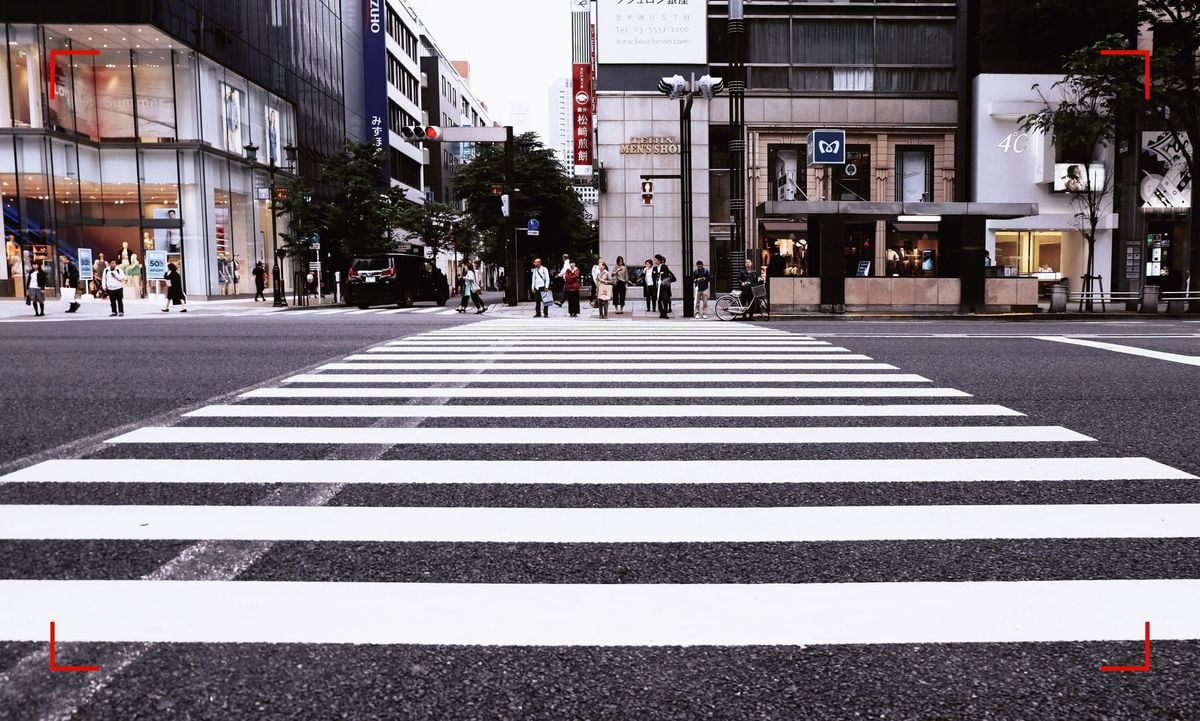 A crosswalk going over a wide street in a city downtown. Pedestrians and buildings on the other side of the street