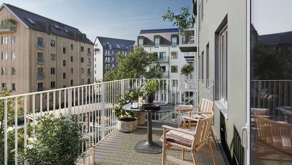 Balcony view of an apartment neighborhood with several wood-clad six-ish story buildings with sloped rooms. Greenery and tables on the balcony; trees visible in the neighborhood.