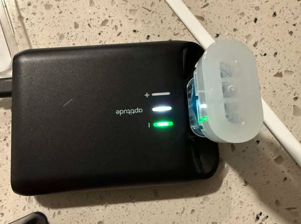 A black plastic Covid test machine. "Aptitude." One unlit line with a +. One line lit up white. One line lit up green with a negative sign. Container of blue fluid.