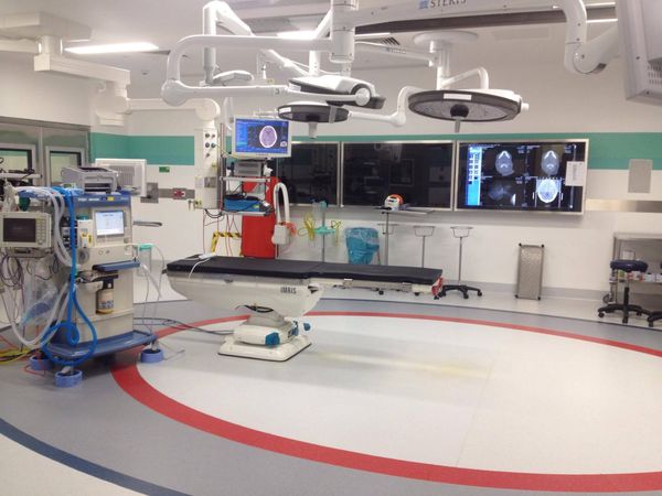 A surgical procedure room with a table, movable bright lights, and brain imaging on screens