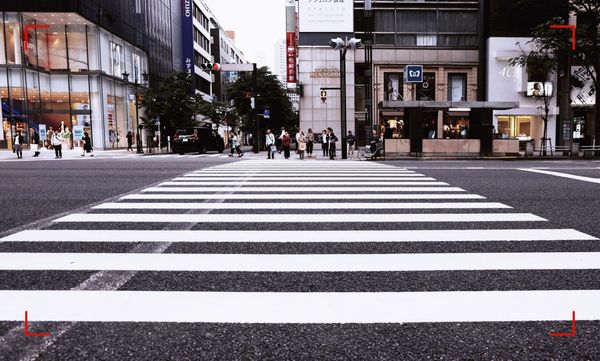 A crosswalk going over a wide street in a city downtown. Pedestrians and buildings on the other side of the street