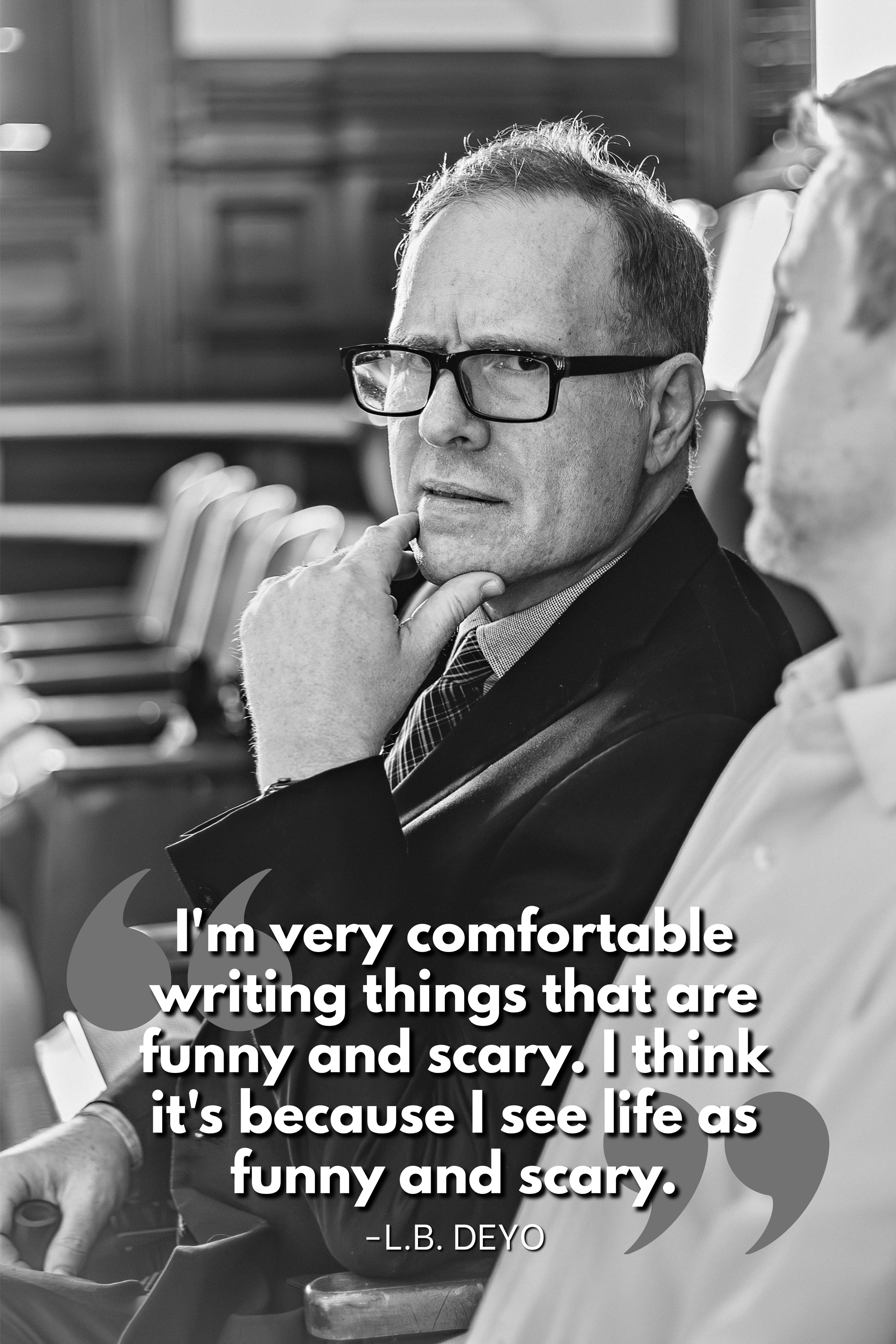 Black-and-white portrait of playwright L.B. Deyo wearing glasses, a suit, and a tie, resting his chin on his hand. Overlaid text reads: “I'm very comfortable writing things that are funny and scary. I think it's because I see life as funny and scary.” — L.B. Deyo