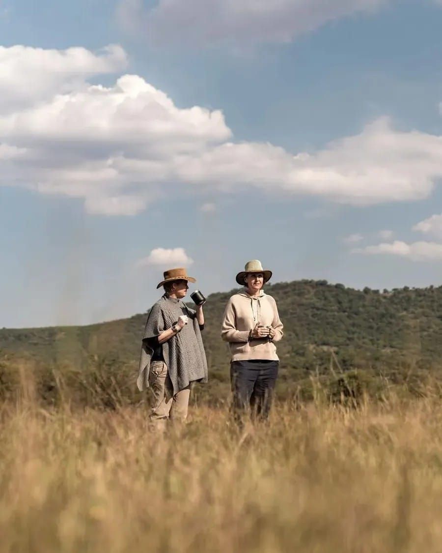 Vikki Jackson and Sian Loehrer standing in long grass at Babohi, Qwabi Private Game Reserve, coffee in hand