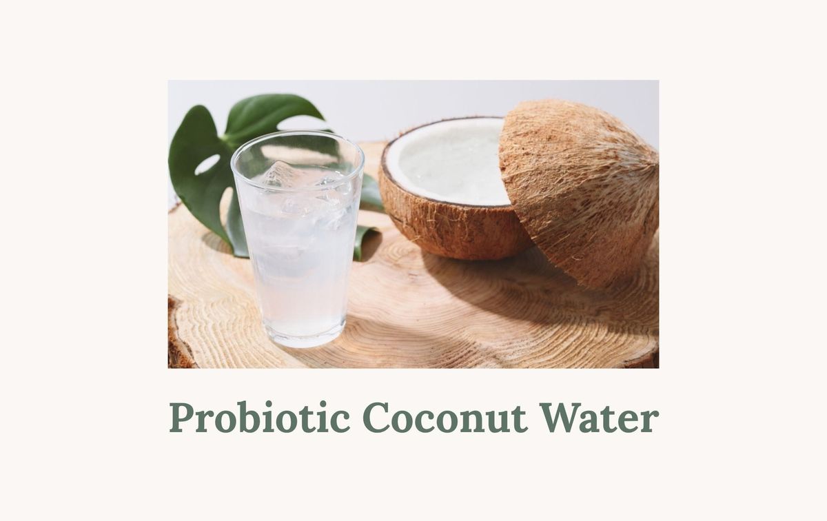 A glass of coconut water with ice and a halved coconut on a wooden surface