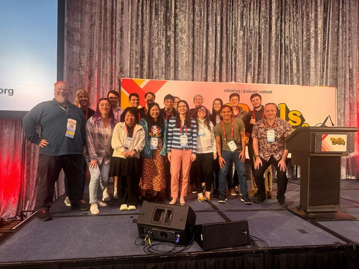 A large group posing together on stage at a RailsConf event