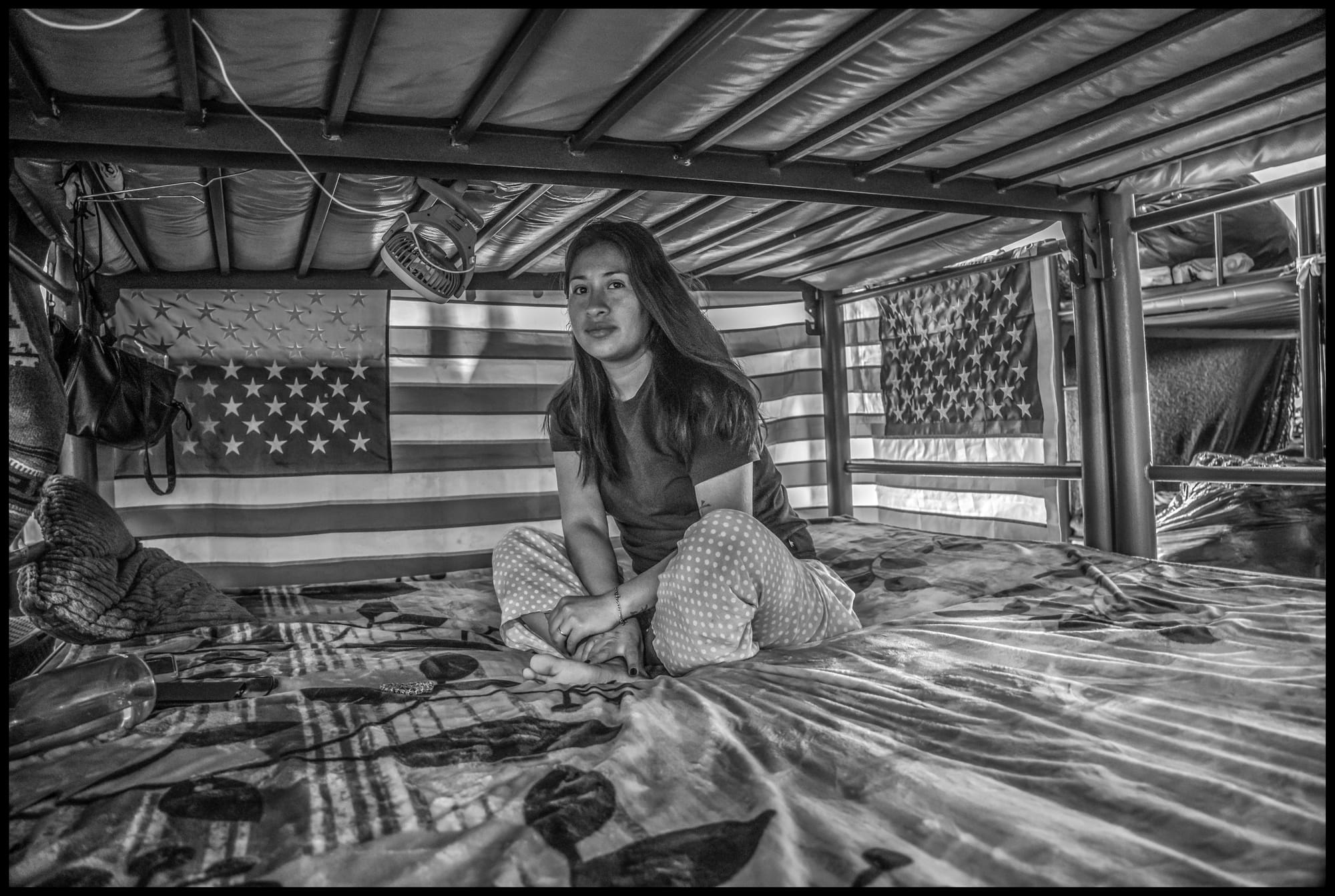 A young woman rests in her bunk at the casa. She uses American flags for privacy.  All photos © David Bacon.