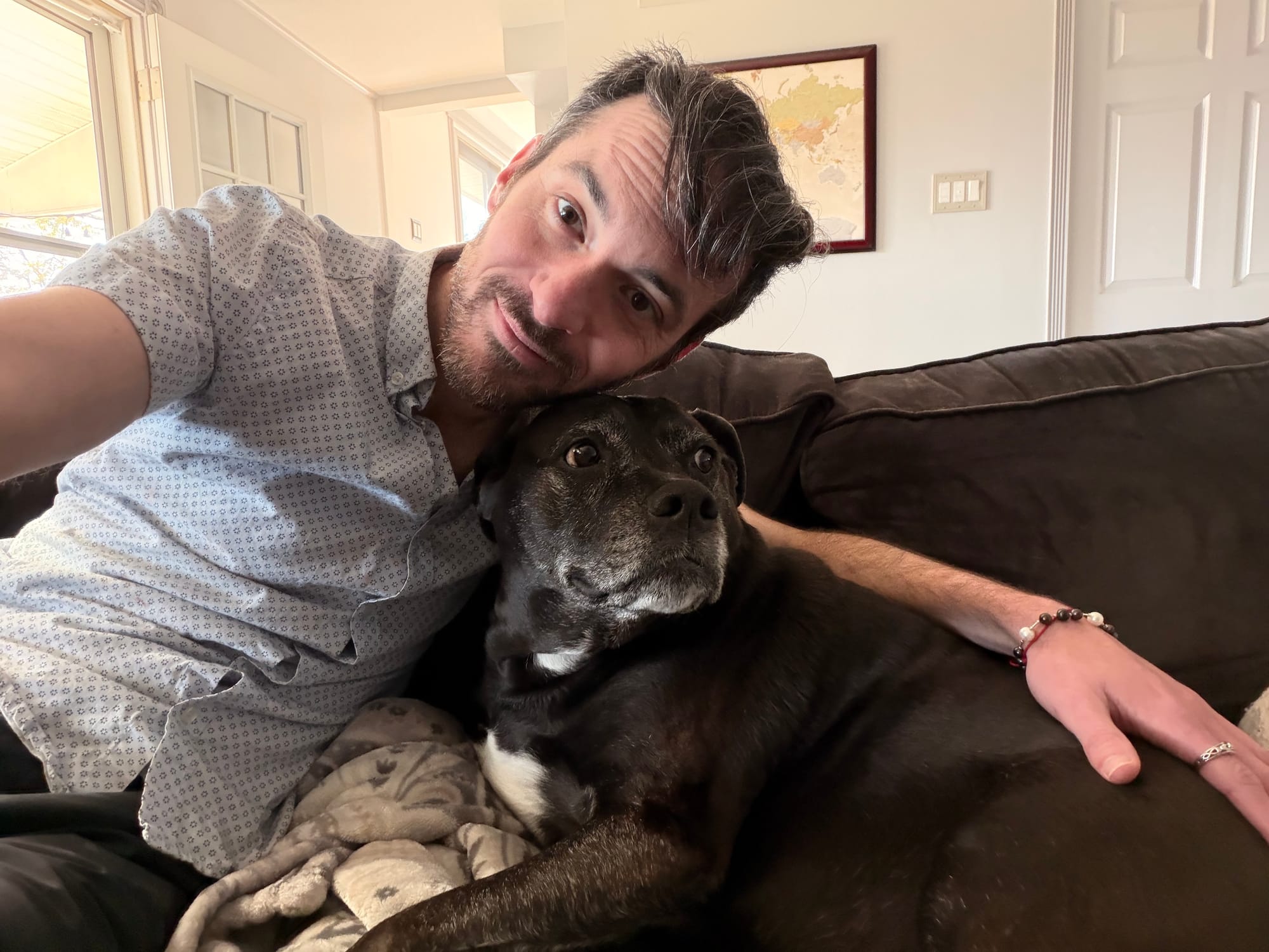 Jason seated next to a black dog on a couch