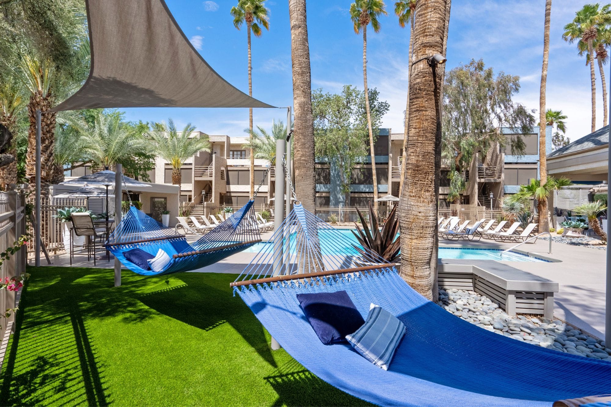 Bright blue hammocks hanging over a patch of Astroturf, adjacent to a sparkling pool, at Beacon at 601 Apartments in Mesa.