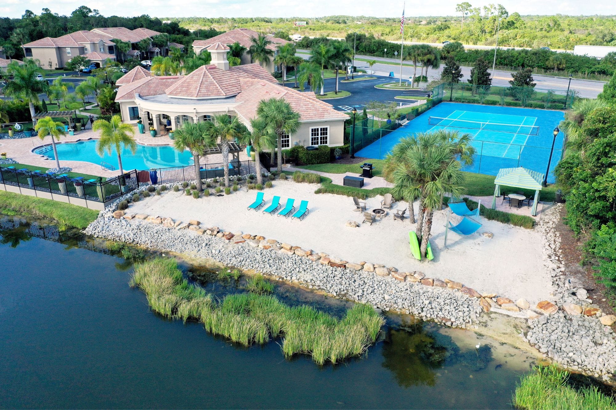 A bird's eye view of the pool, private beach, and tennis court facing the lake at Lakes of Tuscana Apartment community.