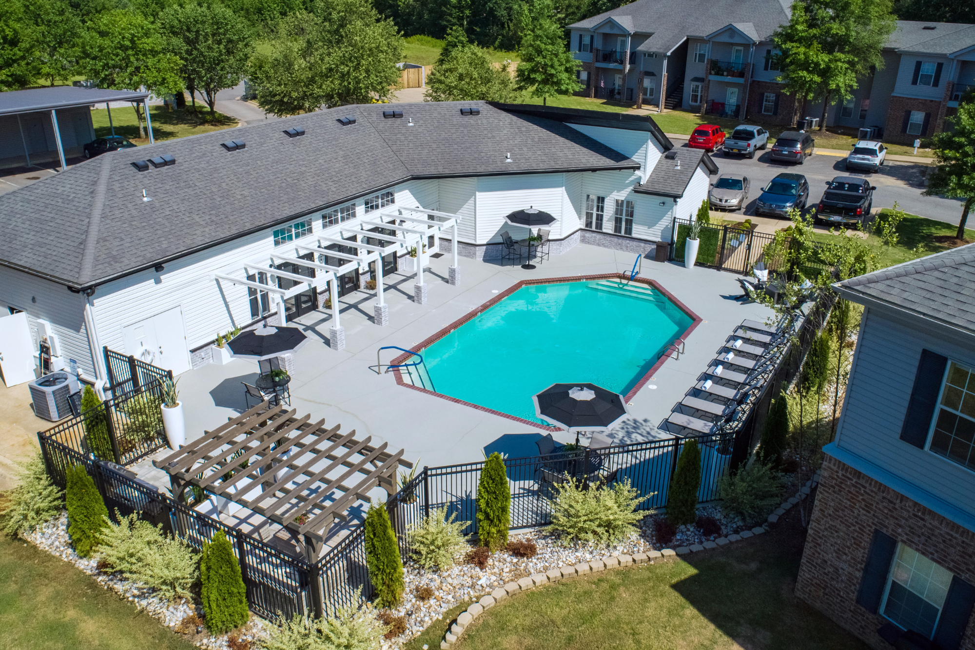 An aerial view of the pool deck at The Avenue Apartments in Cabot, AR - with pergola, poolside loungers, and umbrellas over poolside tables.