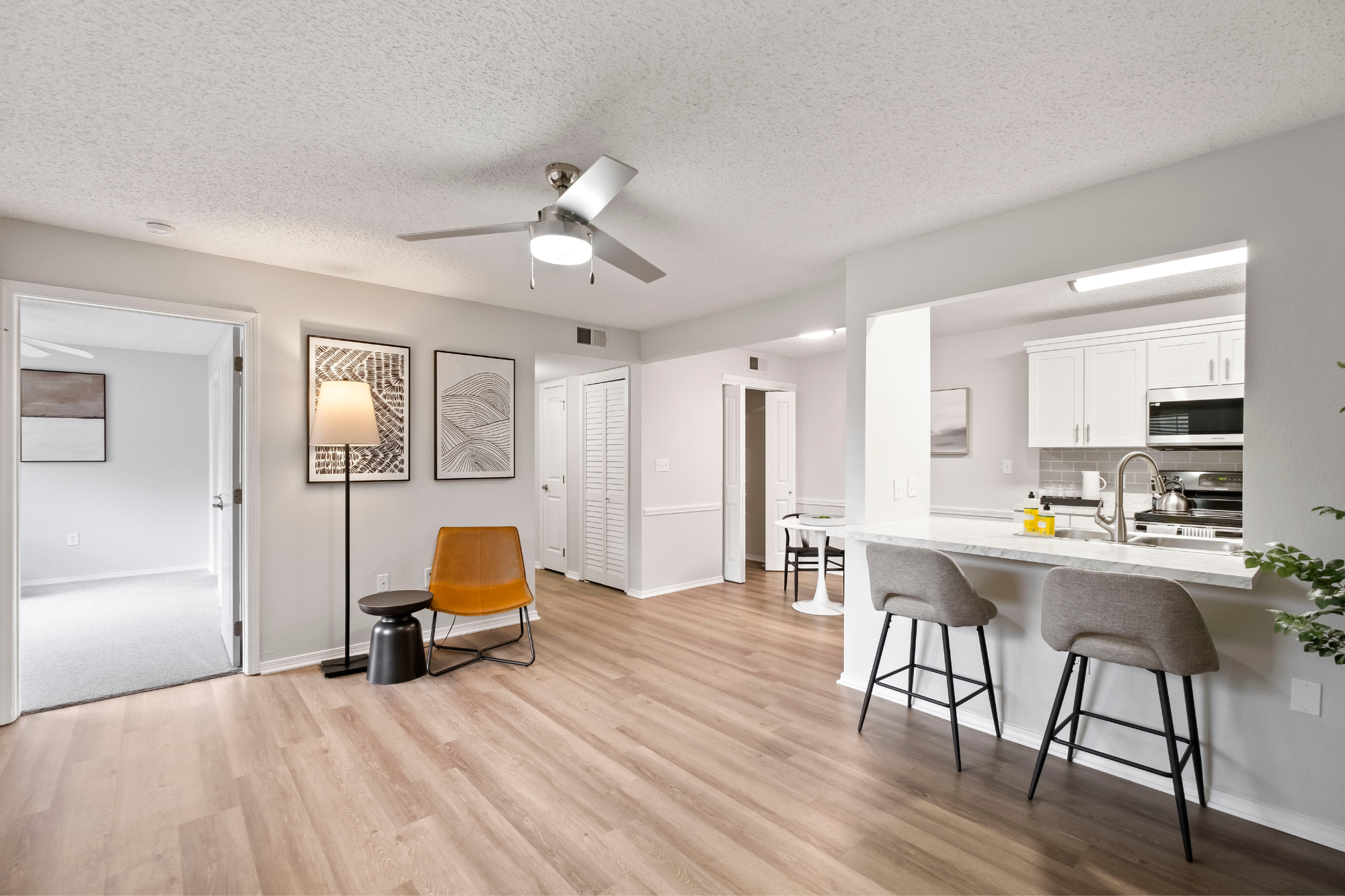 An open-concept apartment floor plan with wood-style flooring throughout, breakfast bar, upgraded kitchen, and ceiling fan.