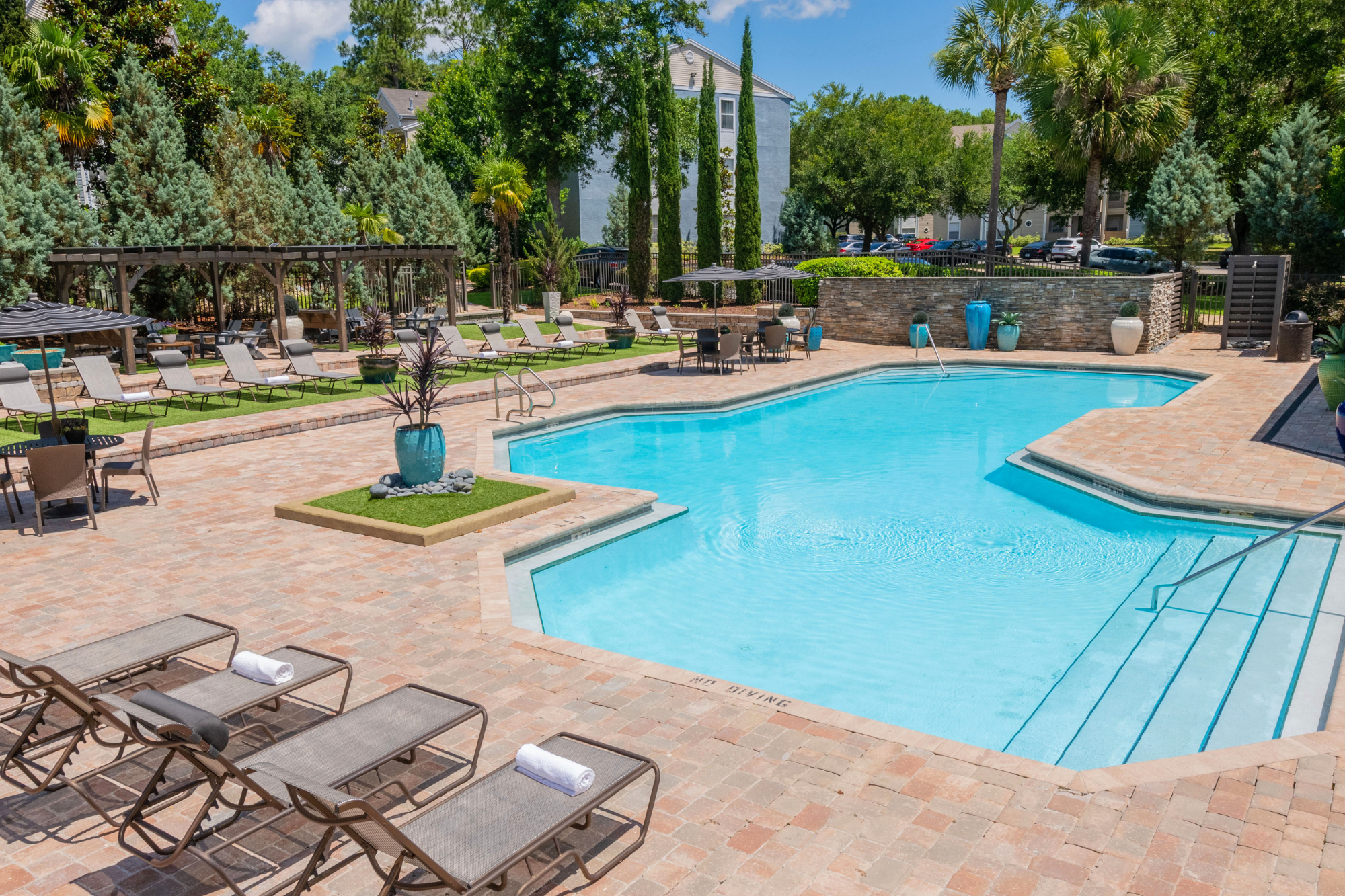 A spacious resort-style pool is surrounded by lounge chairs, and greenery for a calm and relaxing on site experience