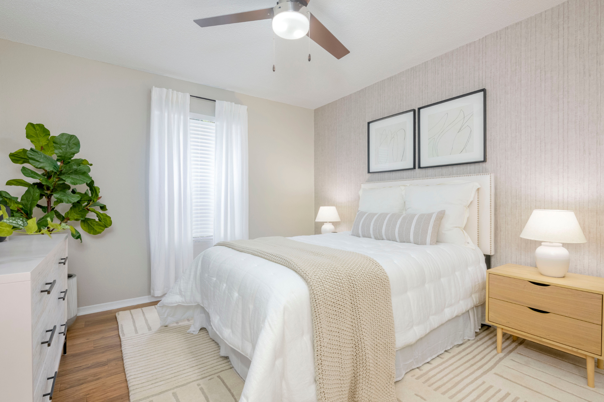 A bright and welcoming bedroom with mostly neutral tones. There is a lamp on either side of the bed and a plant in the corner for some life and pop of color