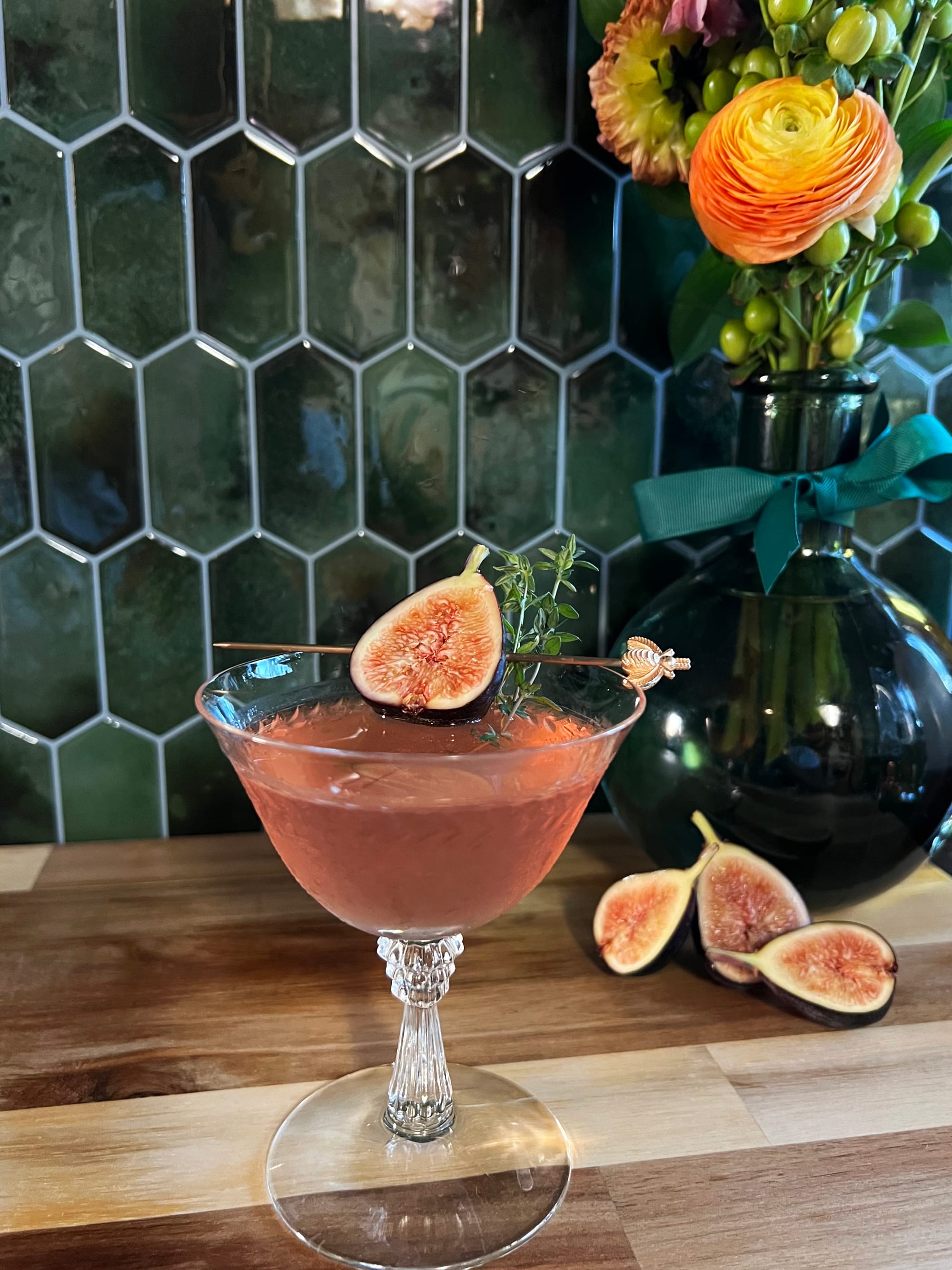 A pinkish cocktail with fruit on a table with a tile background