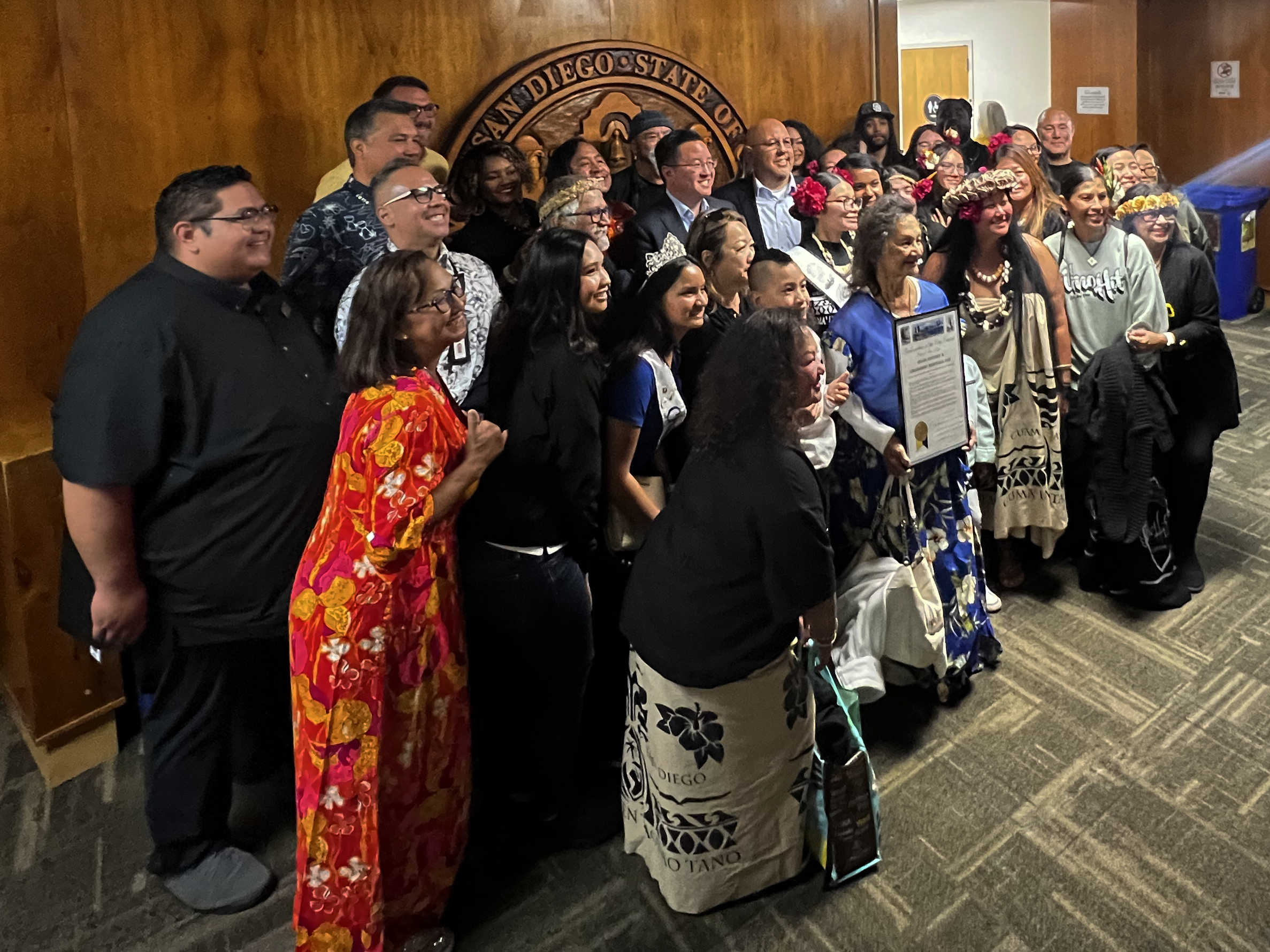 A group of people stand holding the placard proclaiming Guam History and Chamorro Heritage Day