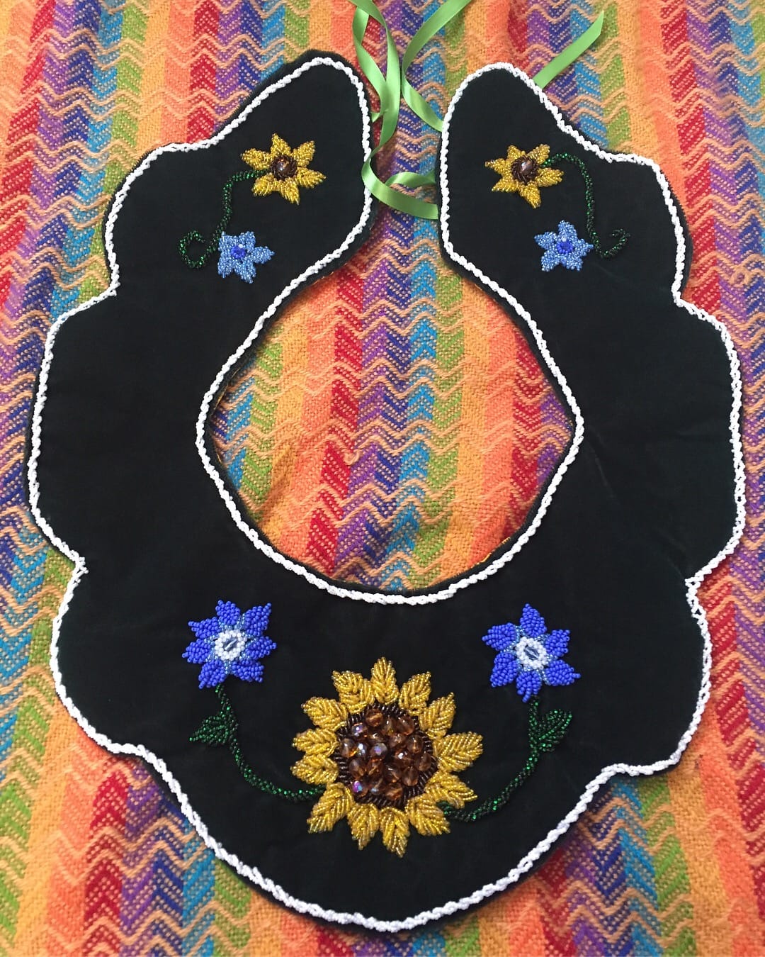 A black beaded neckpiece with yellow and blue flowers on a multicolored table cloth
